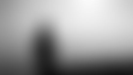 Silhouette of a man standing with arms crossed on a hill, overlooking misty layered mountains in black and white.