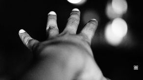 Black-and-white close-up of an outstretched hand with glowing fingertips against blurred lights, moody and abstract.