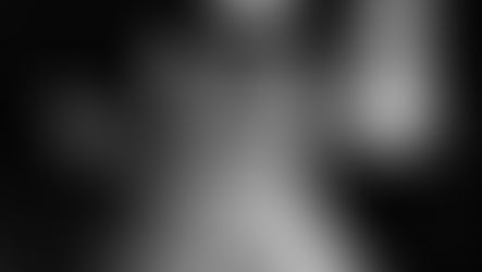 Black-and-white close-up of an outstretched hand with glowing fingertips against blurred lights, moody and abstract.