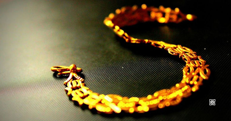 Golden chain bracelet on a dark textured surface, glowing warmly under soft light.