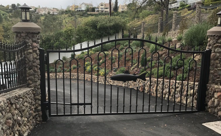 Arched black wrought iron gate with scroll base between stone pillars overlooking the hills in Topanga, CA