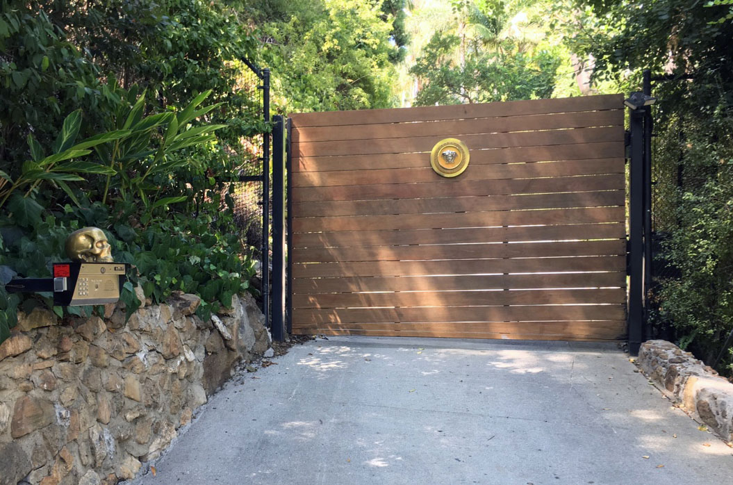 Horizontal wood-slat driveway gate in a black steel frame with brass medallion in Woodland Hills, CA