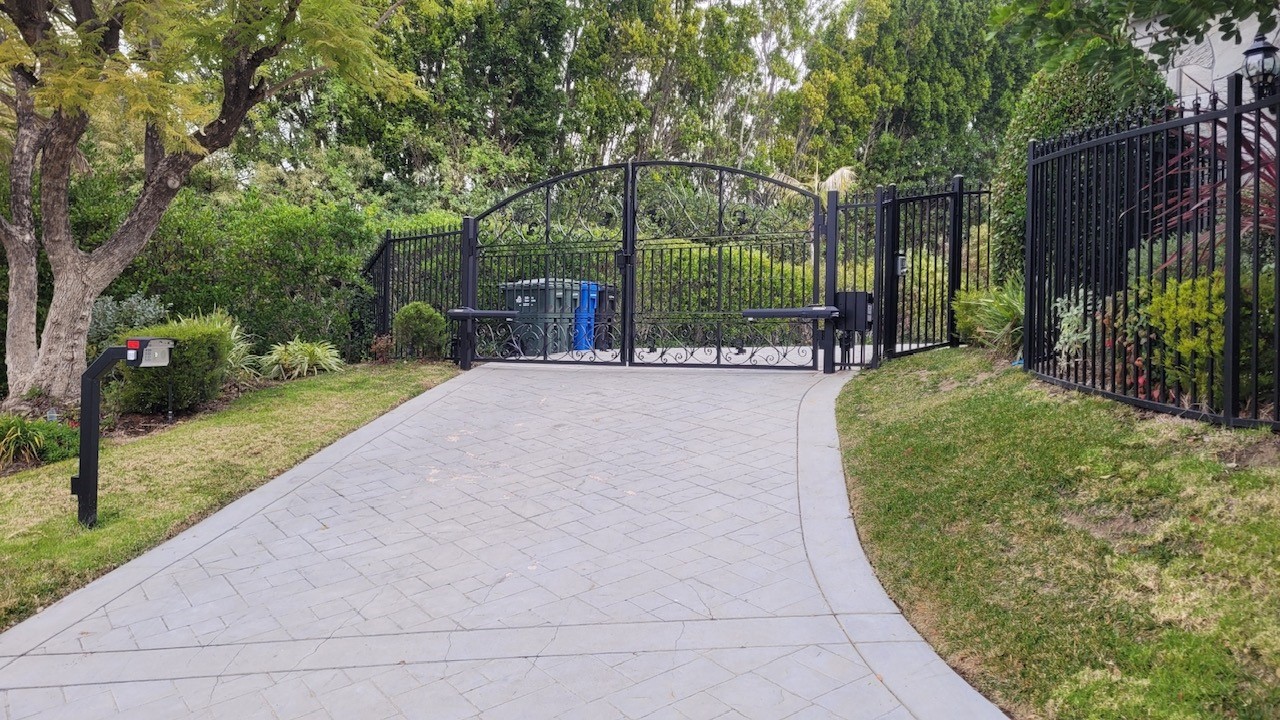 Arched brown solid-panel steel slide gate with lattice top across a residential driveway in Topanga, CA