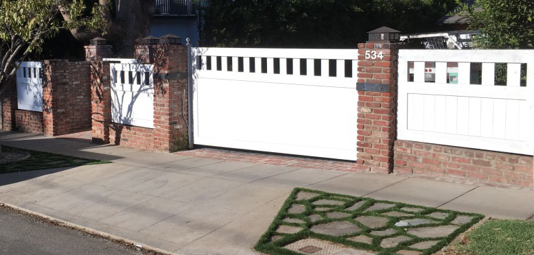 White vinyl slide gate and fence with square cutout top between red brick pillars in Brentwood, CA
