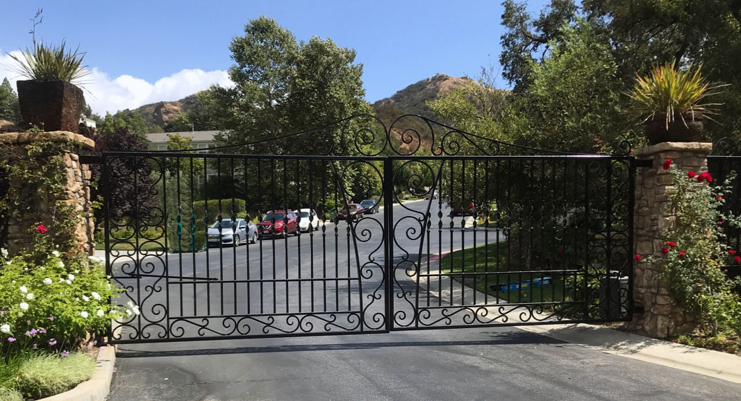 Black wrought iron double driveway gate with scroll base between brick pillars in North Hills, CA