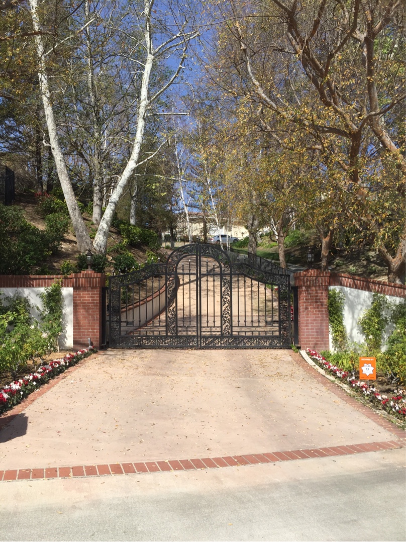 Arched black iron driveway gate between brick pillars at the end of a long driveway in Camarillo, CA
