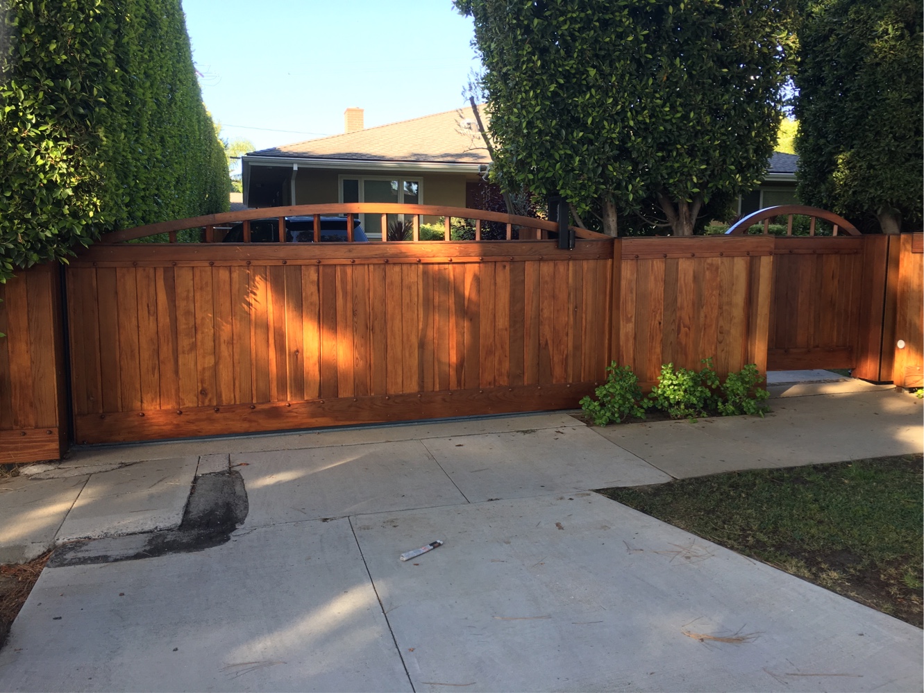 Stained wood double driveway gate with arched lattice top between tall hedges in Santa Monica, CA