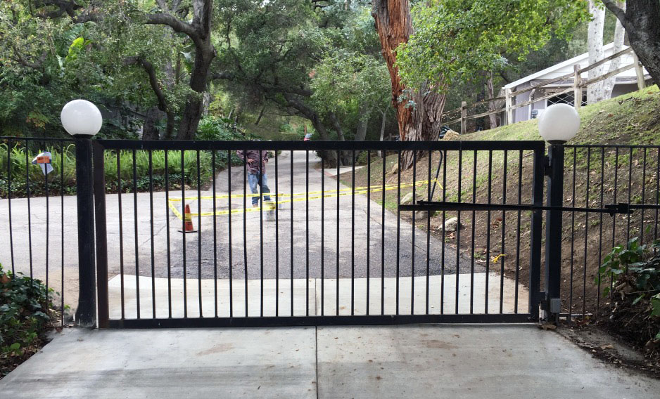 Black iron slide gate between white globe-light posts across a residential street entrance in Agoura Hills, CA