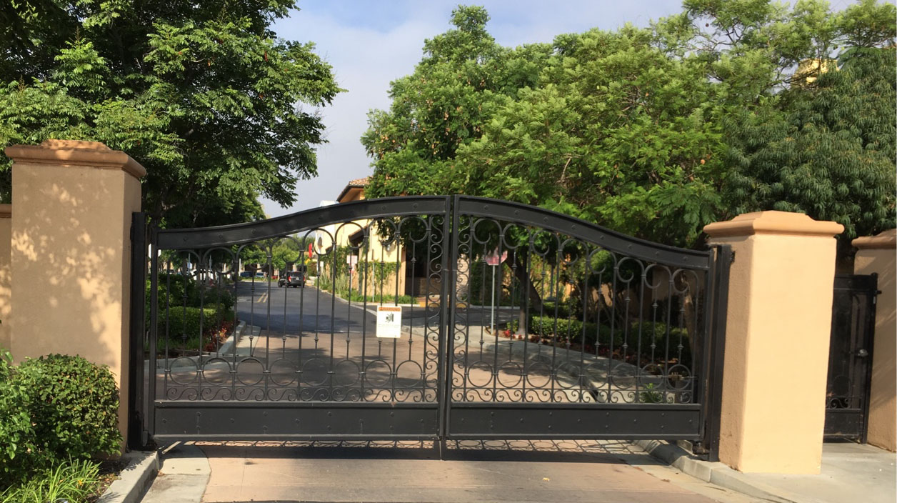 Arched black iron double driveway gate between tan stucco pillars at a residential entry in Agoura Hills, CA