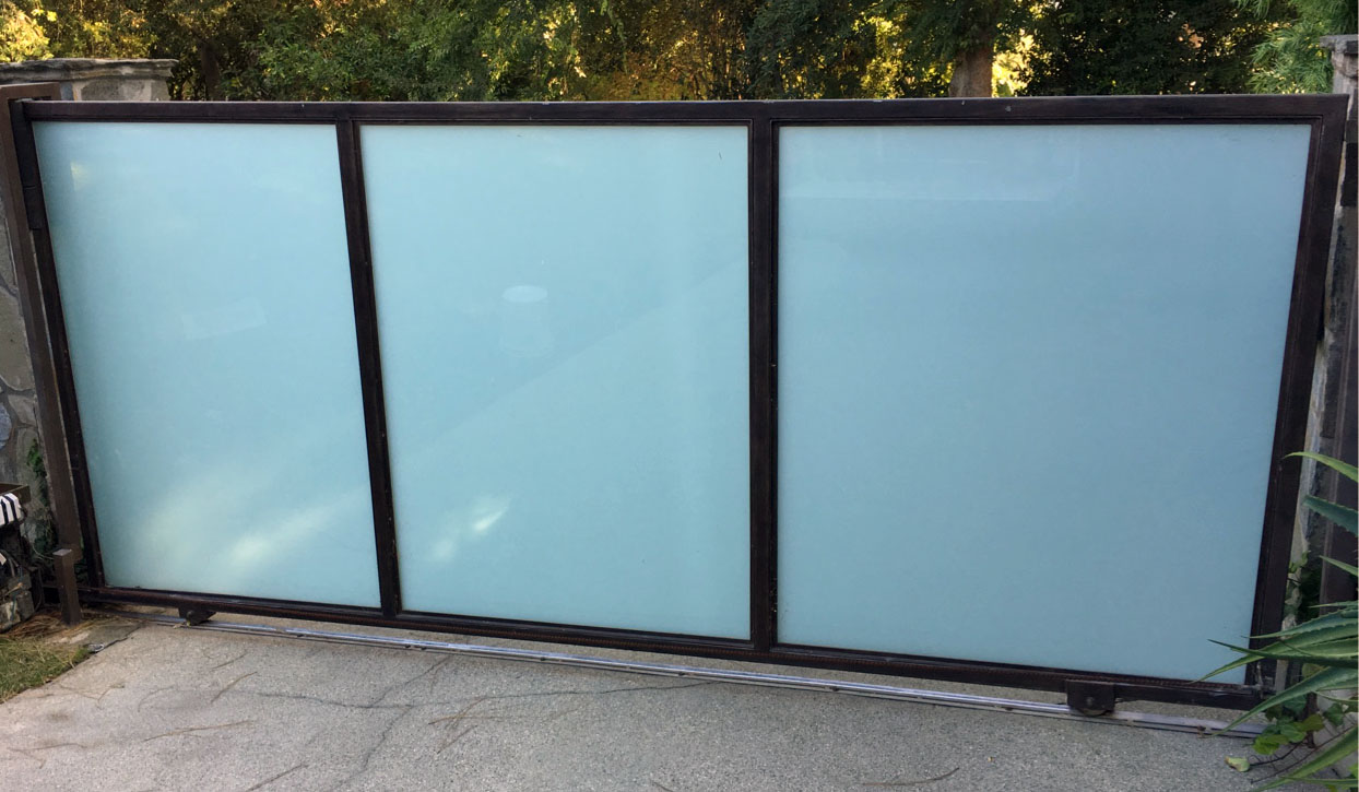 Black steel-frame slide gate with frosted glass panels across a driveway in Santa Monica, CA