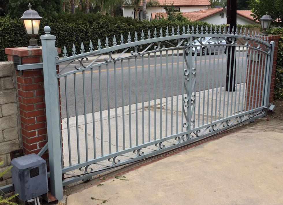 Gray iron slide gate with scroll top and gate operator beside a red brick pillar in Shadow Hills, CA