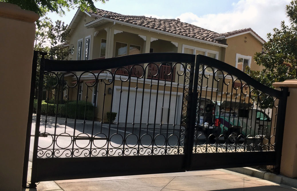 Arched black wrought iron double swing gate with scroll accents at a Mediterranean-style home in Porter Ranch, CA