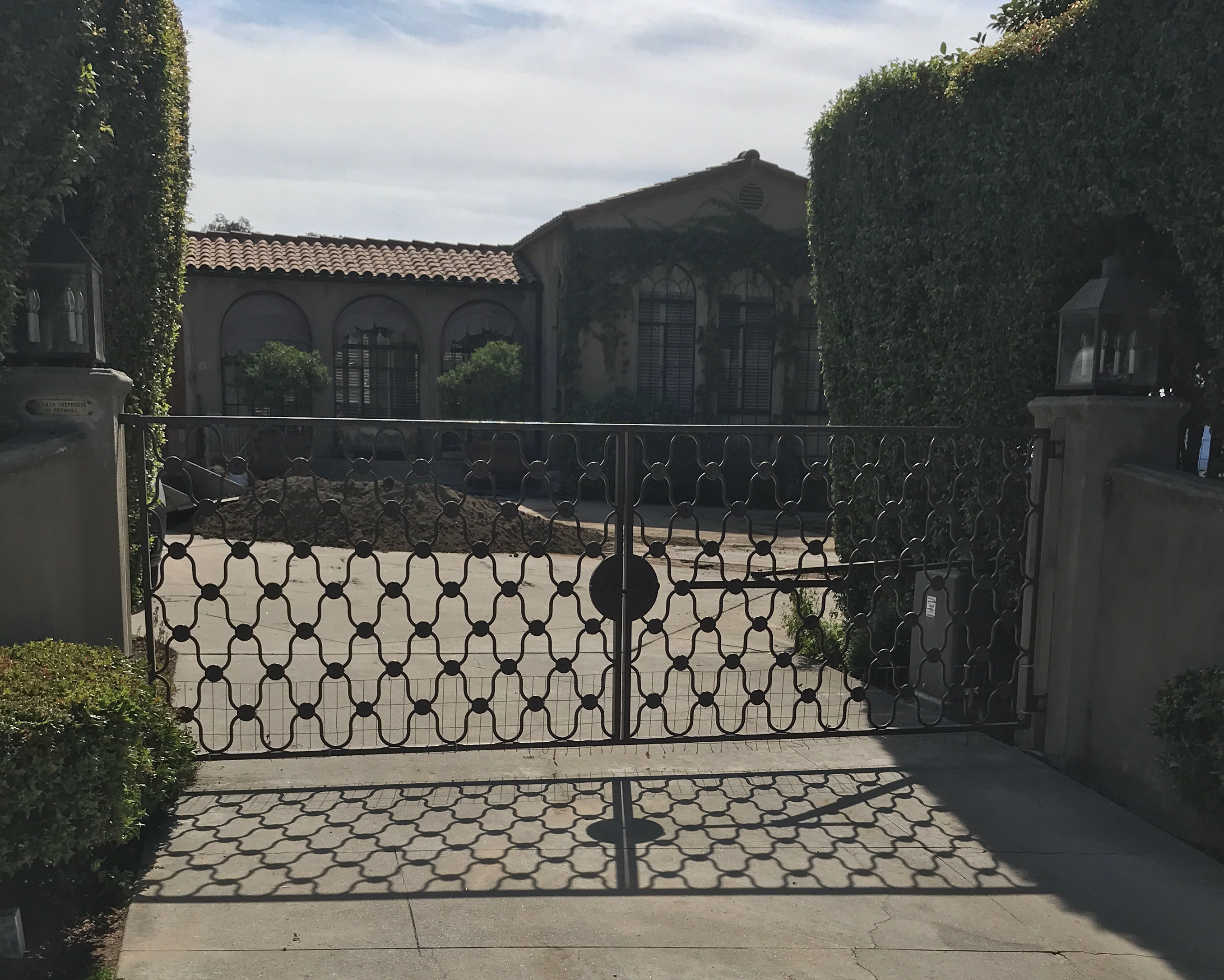 Black wrought iron driveway gate with lattice pattern between stone pillars in Granada Hills, CA