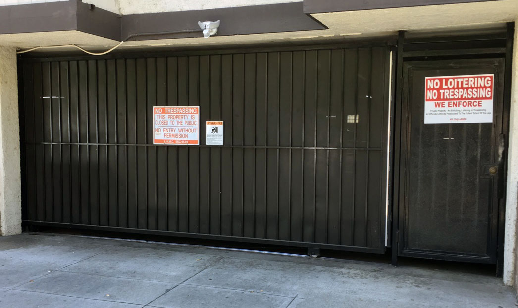 Black steel garage security gate with pedestrian door and no-trespassing signs at an apartment building in Panorama City, CA