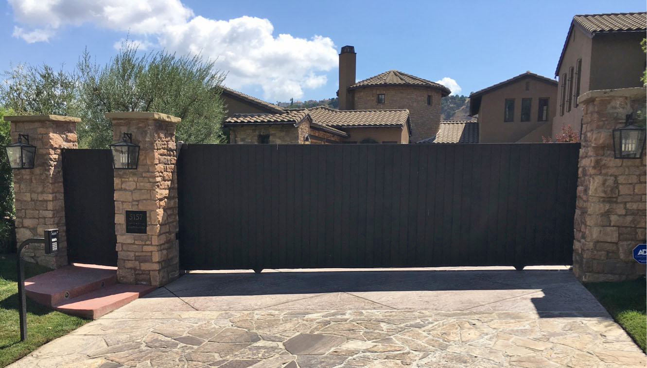 Black solid steel slide gate between stone pillars with lanterns at a Tuscan-style estate in West Hills, CA