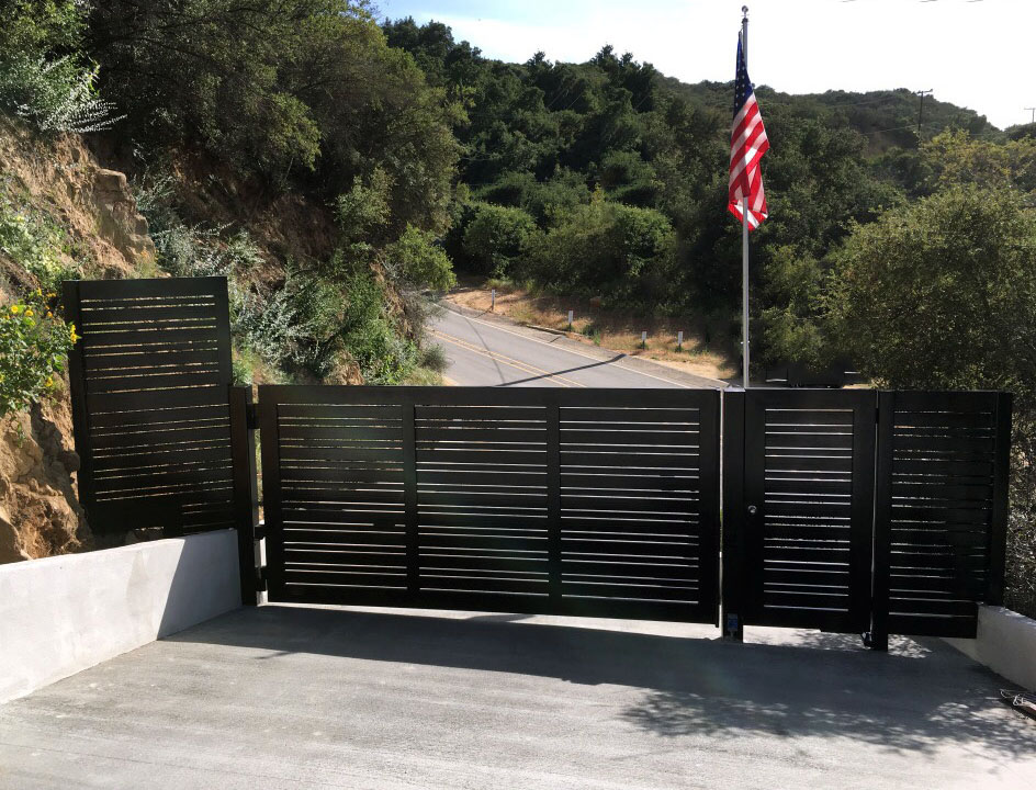Black horizontal-slat steel double gate across a hillside driveway in North Hills, CA