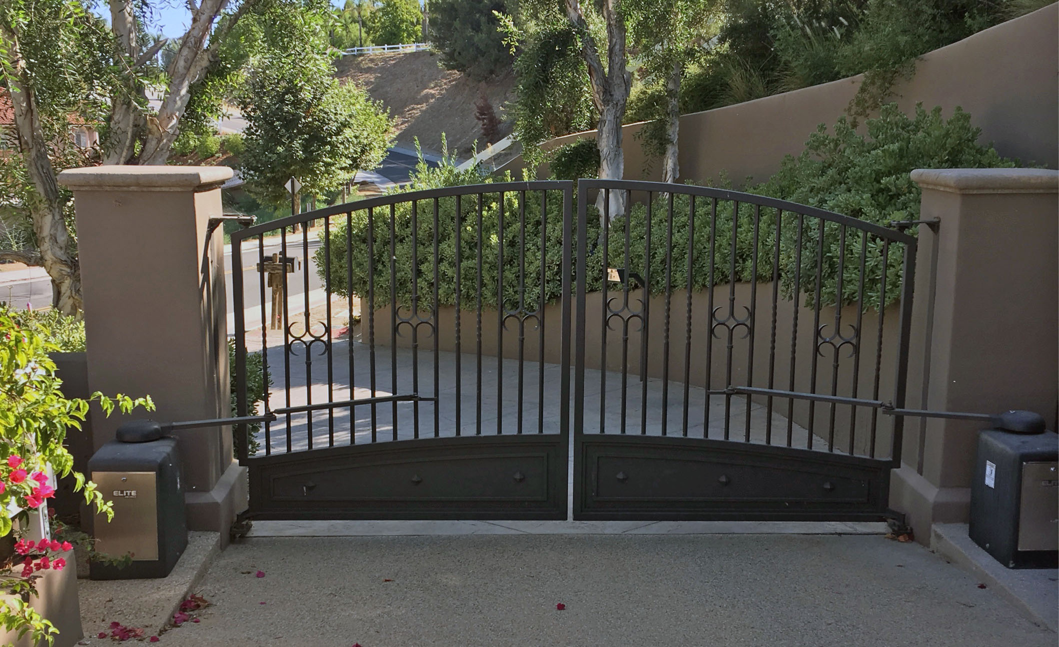 Arched black wrought iron double gate between tan stucco pillars at a residential entry in Camarillo, CA