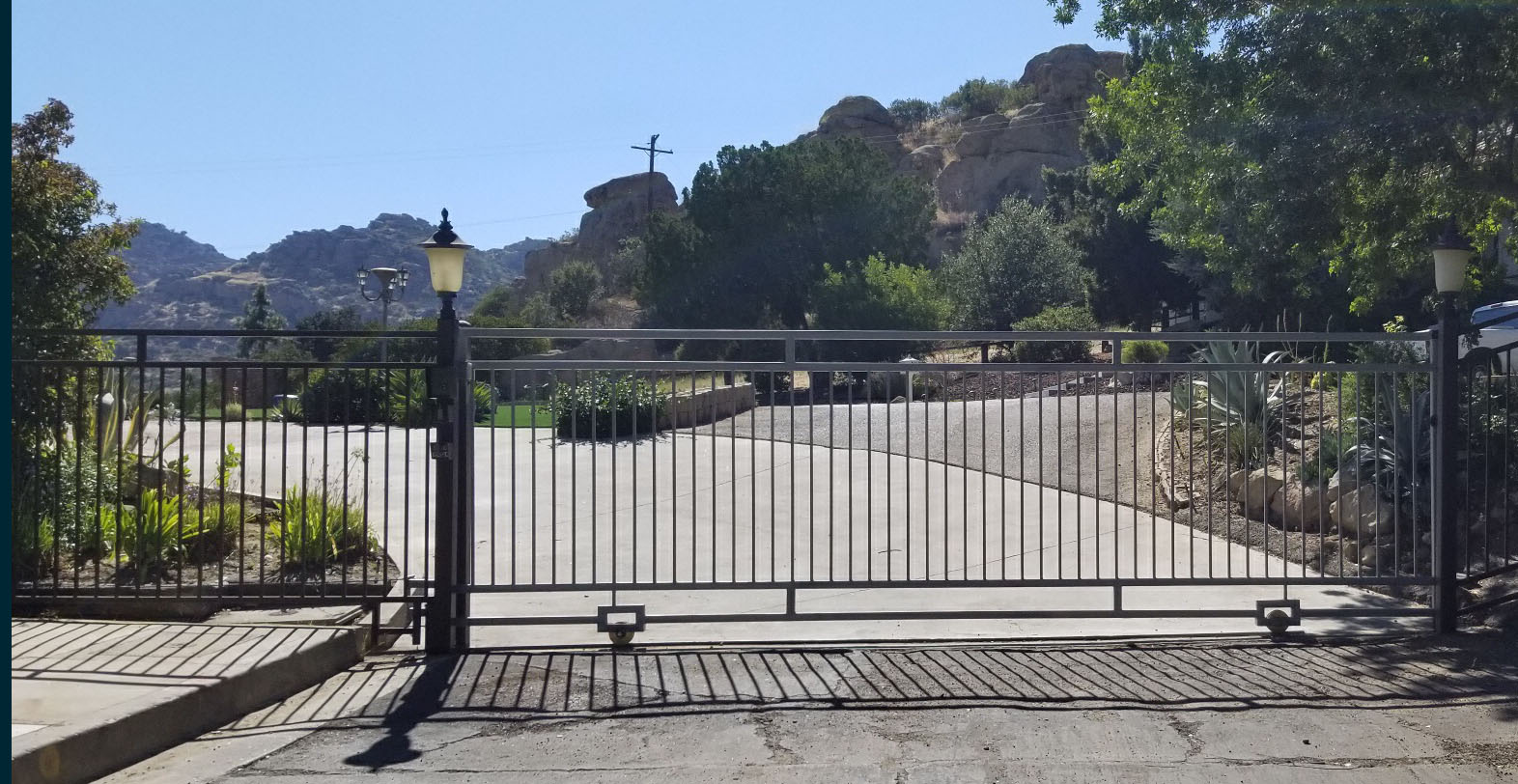 Black iron slide gate across a wide driveway with rocky mountain views in Shadow Hills, CA