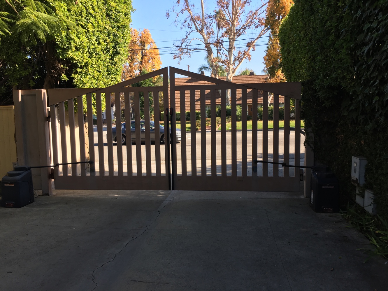 Arched dark wood-slat double driveway gate between stucco pillars in Encino, CA