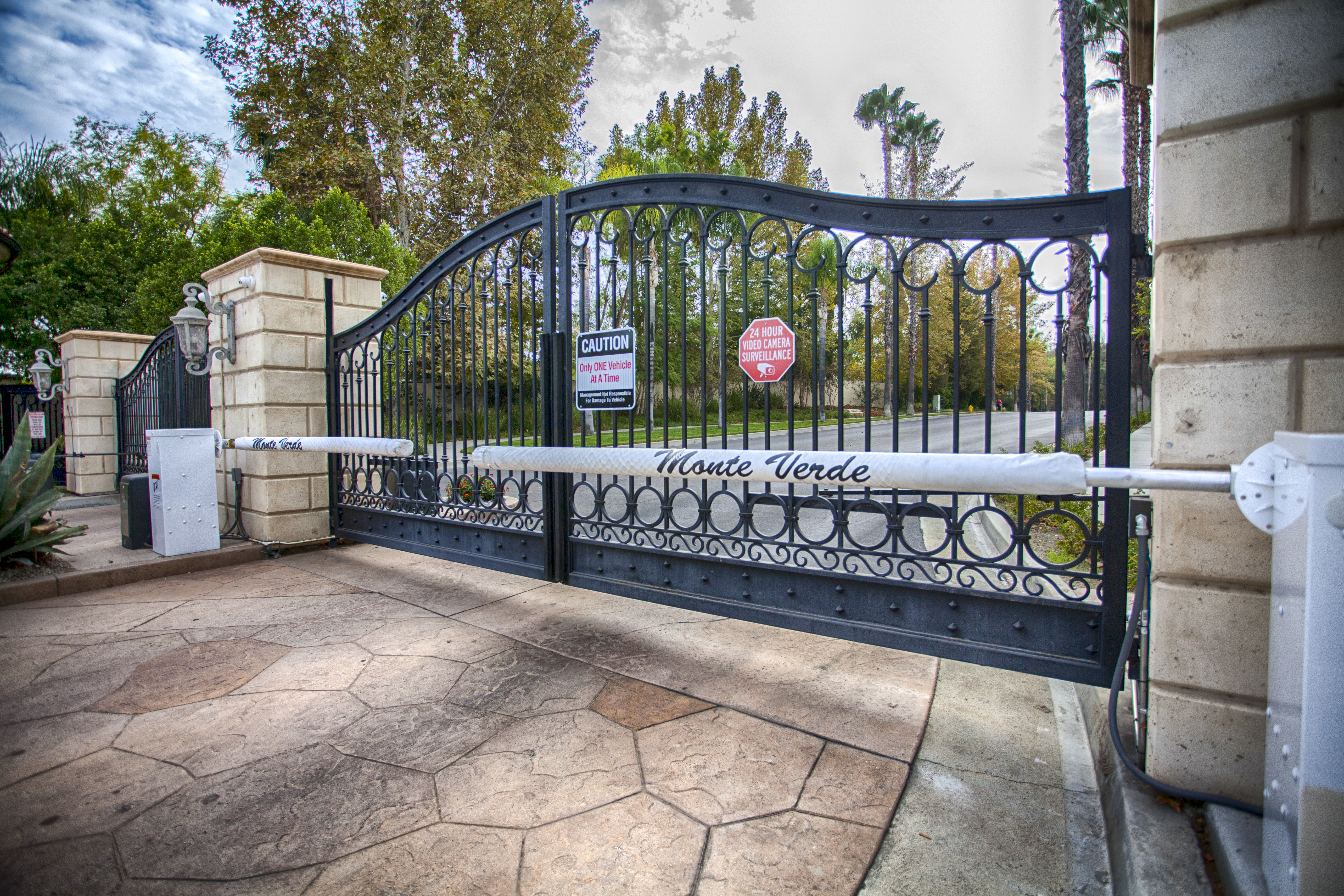Arched black iron community entry gate with barrier arm and decorative ring panels in Reseda, CA