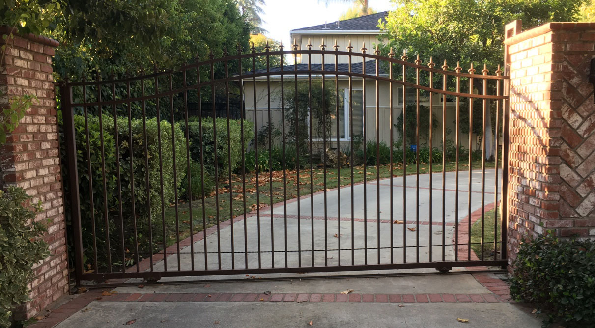 Arched black iron slide gate between brick pillars across a residential driveway in West Hills, CA