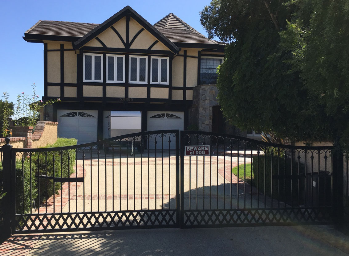 Black iron fence and driveway gate in front of a Tudor-style home in Woodland Hills, CA