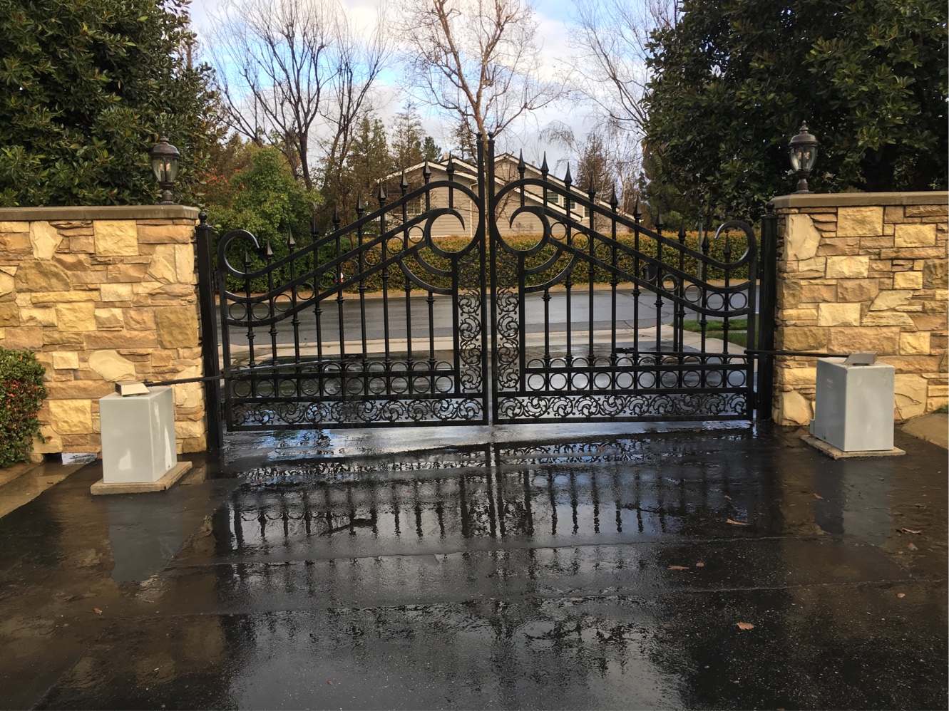 Arched black wrought iron double driveway gate with scroll design between stacked-stone pillars in Moorpark, CA