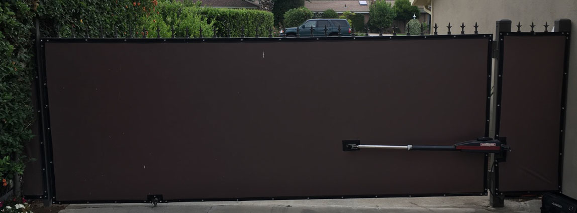 Brown solid privacy slide gate with swing gate operator arm along a hedge in Valley Glen, CA