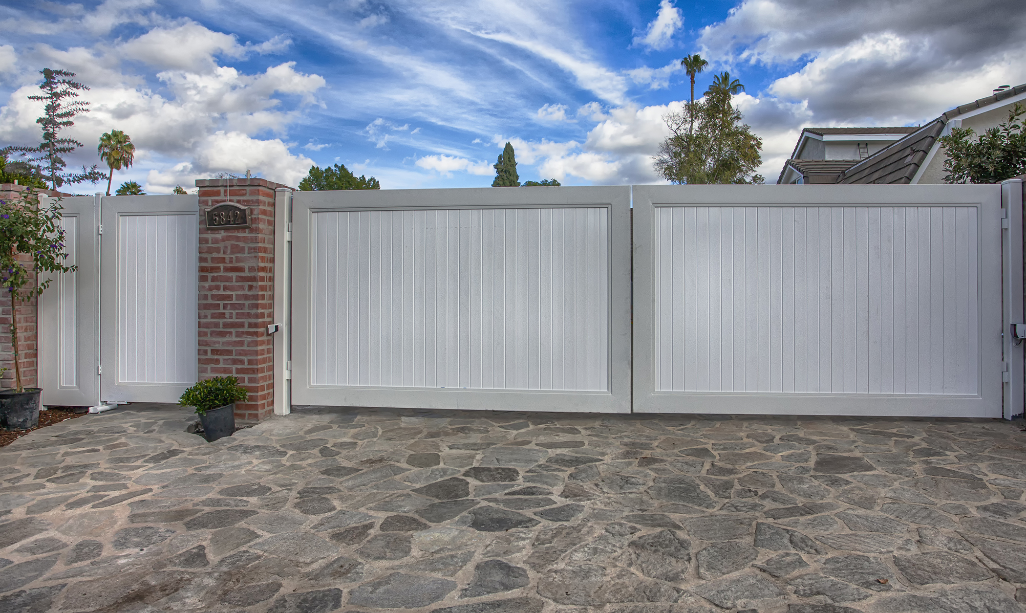 White vinyl privacy driveway gate with brick pillar over a paver driveway in Sherman Oaks, CA