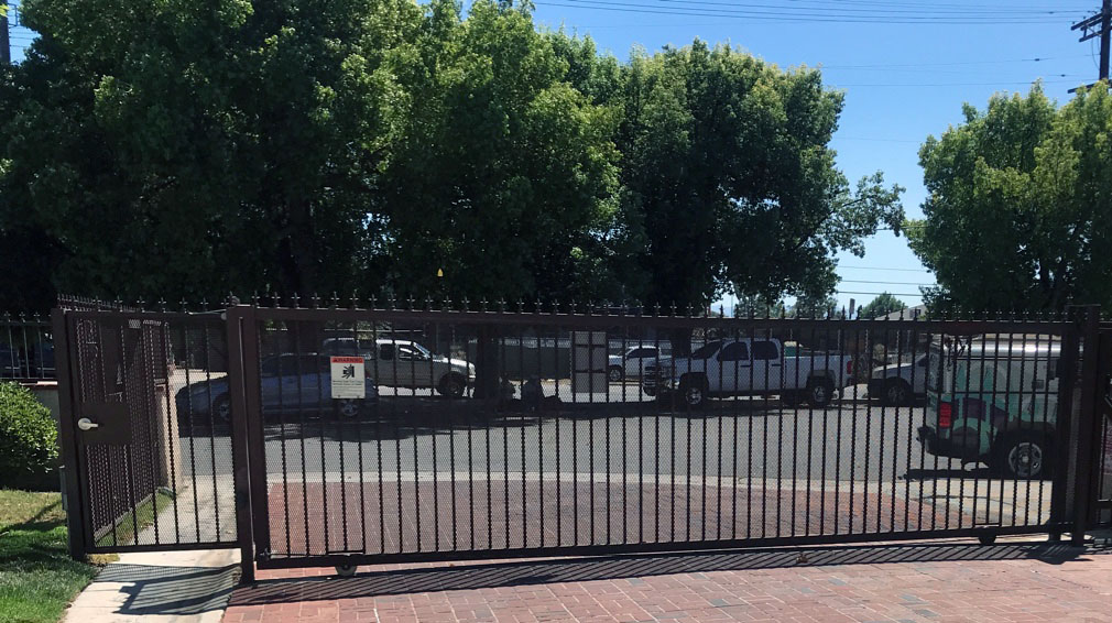 Black iron slide gate with spear-top pickets at a parking lot entrance in Sunland, CA