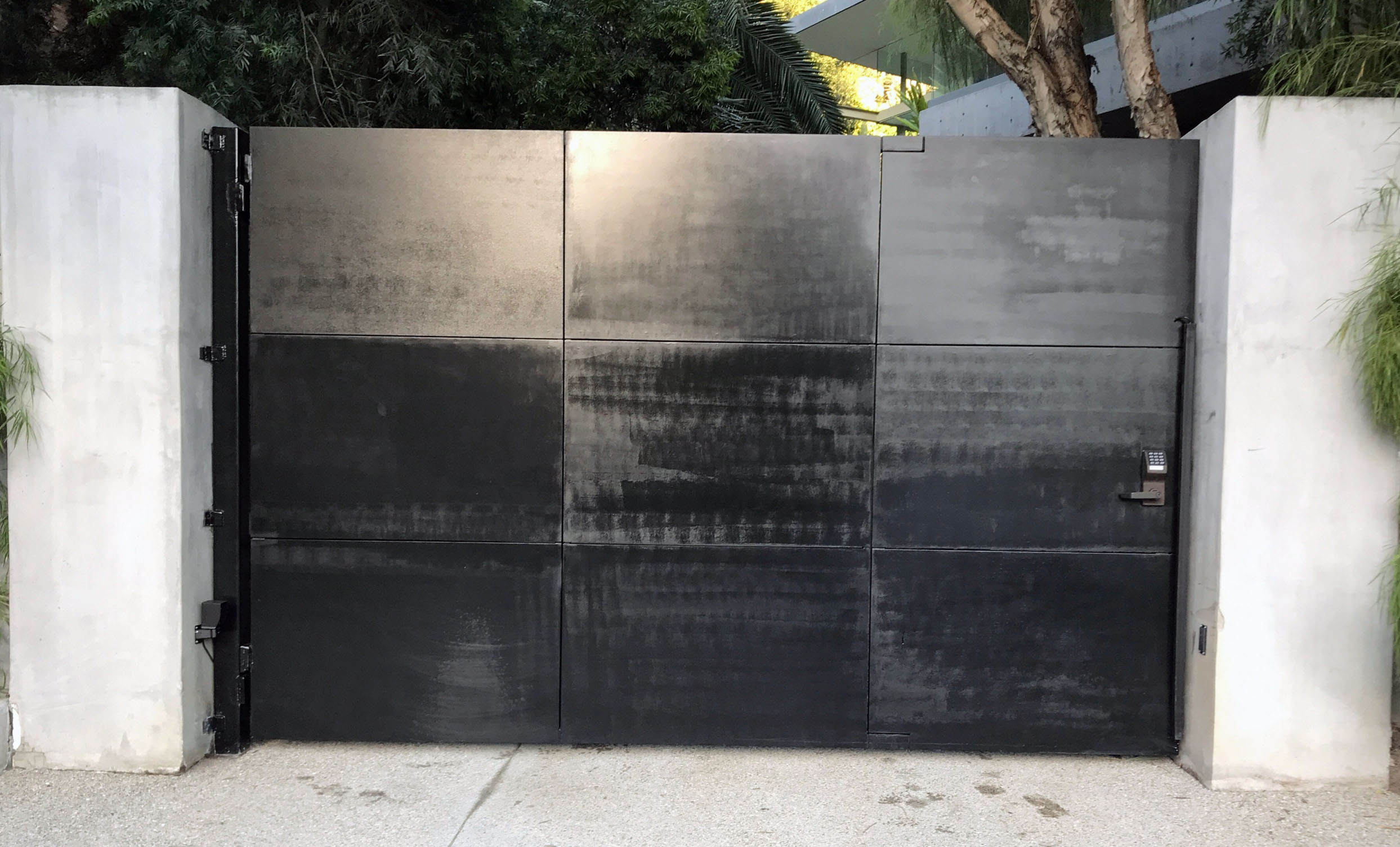 Black solid steel-plate double driveway gate between white stucco pillars in Hollywood, CA