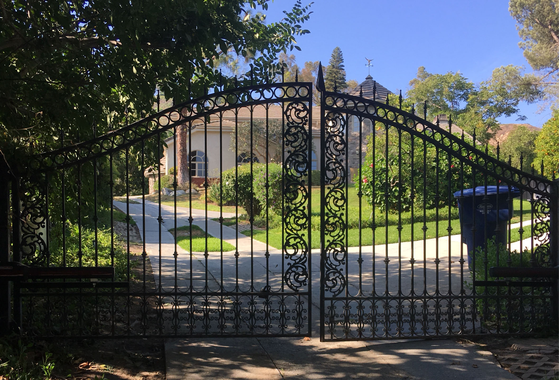 Arched black wrought iron double driveway gate with ornate scroll panels at an estate in Porter Ranch, CA