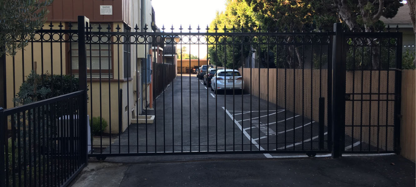 Black iron double swing gate with spear-top pickets at an apartment driveway entrance in Chatsworth, CA