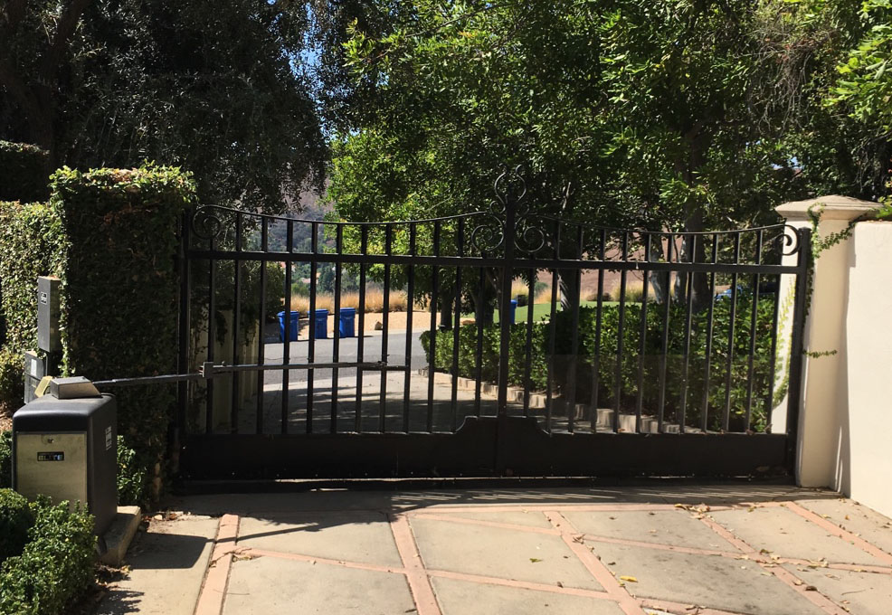 Black iron slide gate with gate operator between stone pillars at a tree-lined driveway in Calabasas, CA