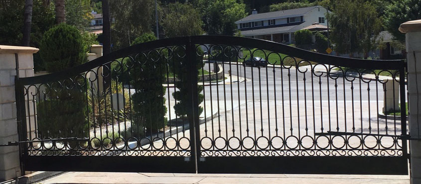 Arched black wrought iron driveway gate with scroll design overlooking a hillside neighborhood in Shadow Hills, CA