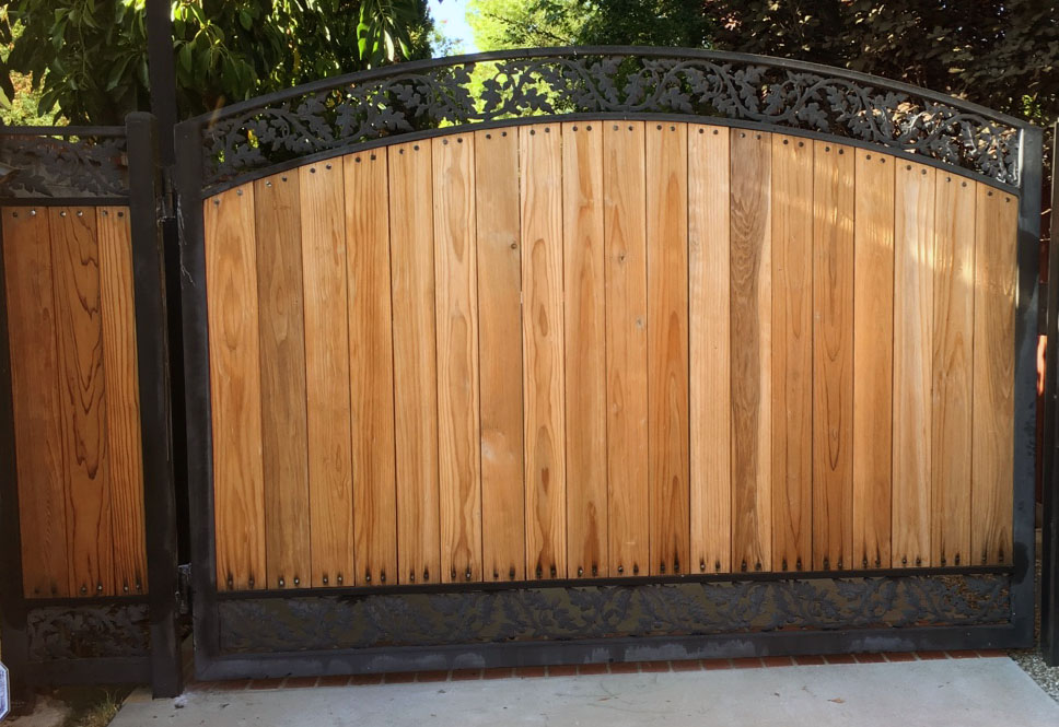 Arched natural wood driveway gate in a black steel frame with scroll top trim in Eagle Rock, CA