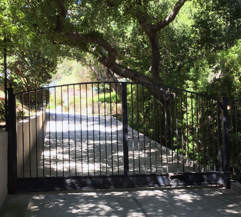 Black iron swing gate across a shaded canyon driveway under oak trees in Topanga, CA