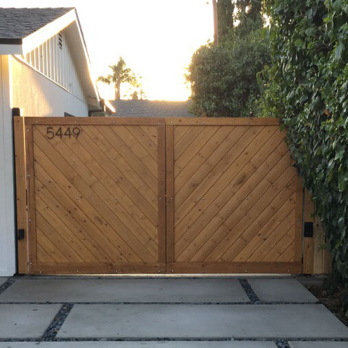 Natural wood driveway gate with diagonal plank pattern beside a hedge-lined driveway in West Hills, CA