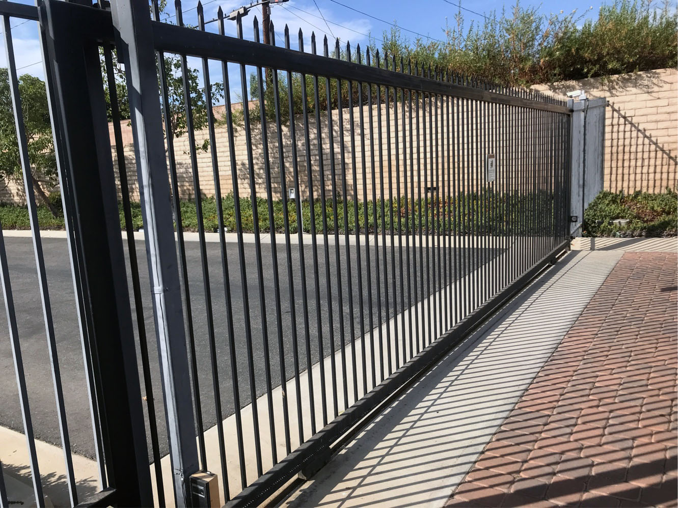 Black iron slide gate with spear-top pickets along a brick paver driveway in Panorama City, CA
