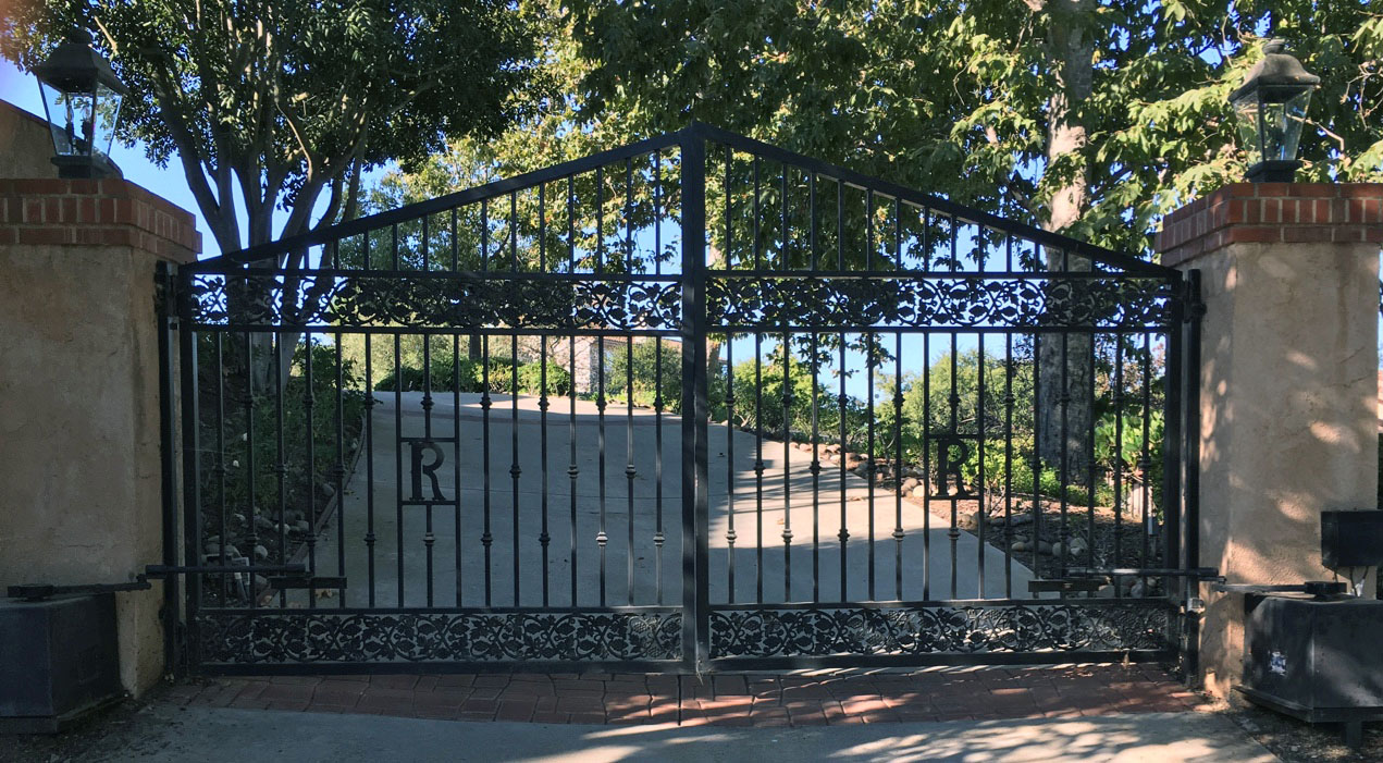 Arched black wrought iron double driveway gate with monogram letters and ornate base in Calabasas, CA