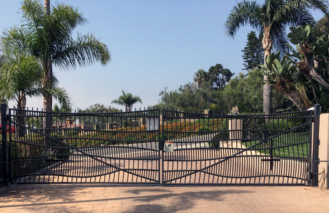 Black iron ranch slide gate with crossed-bar design at a palm-lined estate driveway in Somis, CA