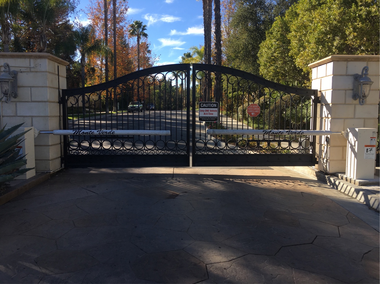 Arched black wrought iron slide gate with barrier arm between stone pillars at a community entrance in Pasadena, CA