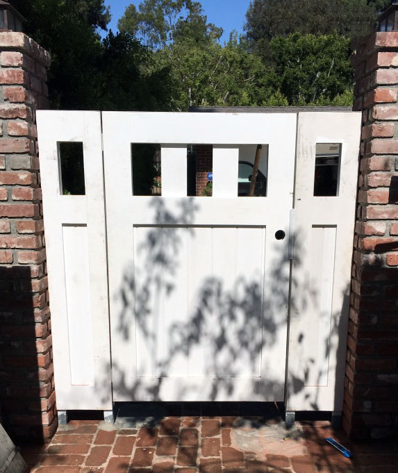 White pedestrian gate with square window cutouts set in a red brick wall in Brentwood, CA