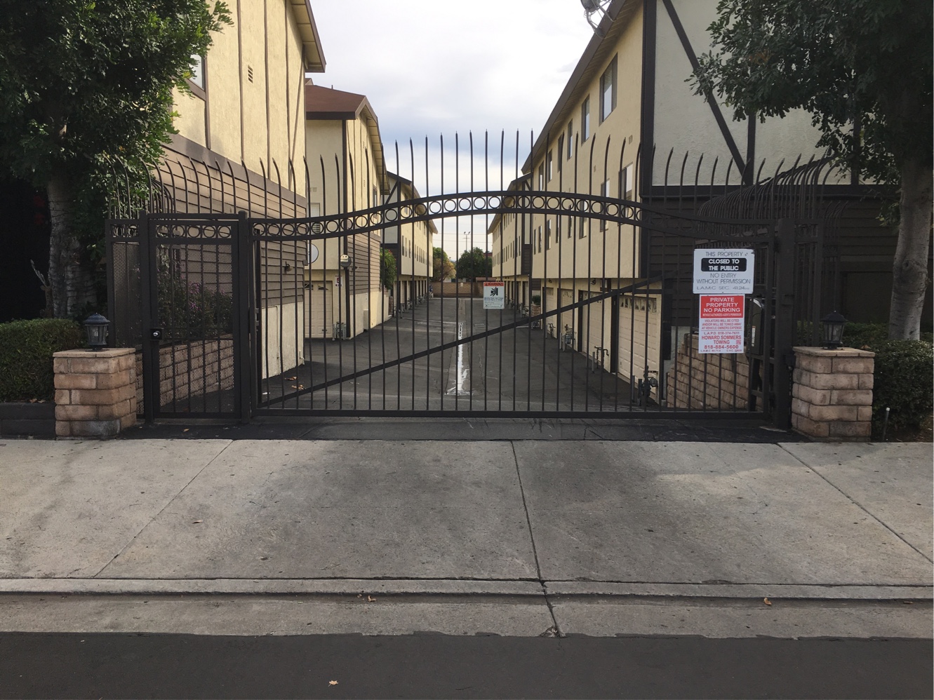 Arched black iron slide gate at an apartment complex driveway between brick planters in Encino, CA