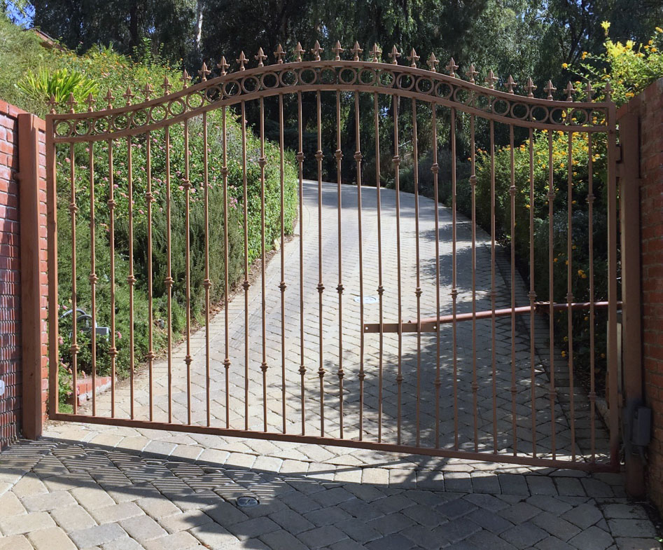 Arched black iron double swing gate between brick pillars on a paver driveway in Tarzana, CA
