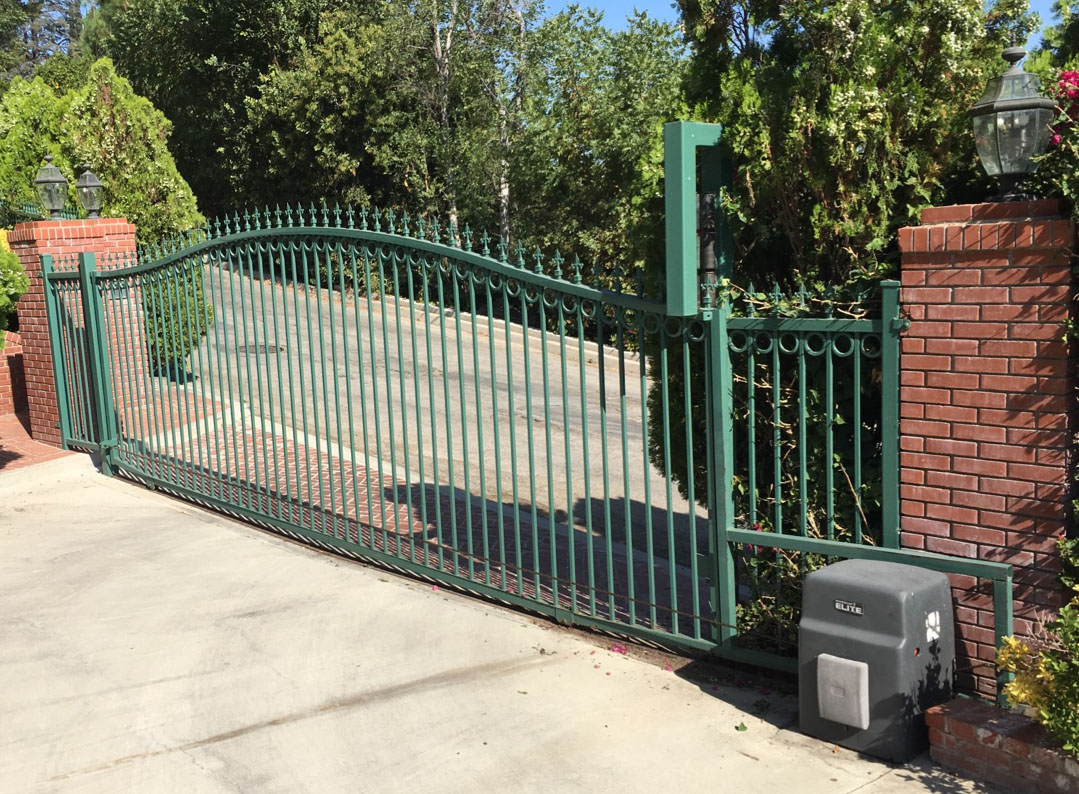 Arched green iron slide gate with gate operator between red brick pillars in Pasadena, CA