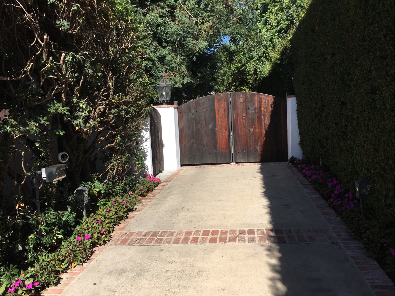 Arched dark wood double driveway gate between white stucco pillars at the end of a hedge-lined driveway in Thousand Oaks, CA