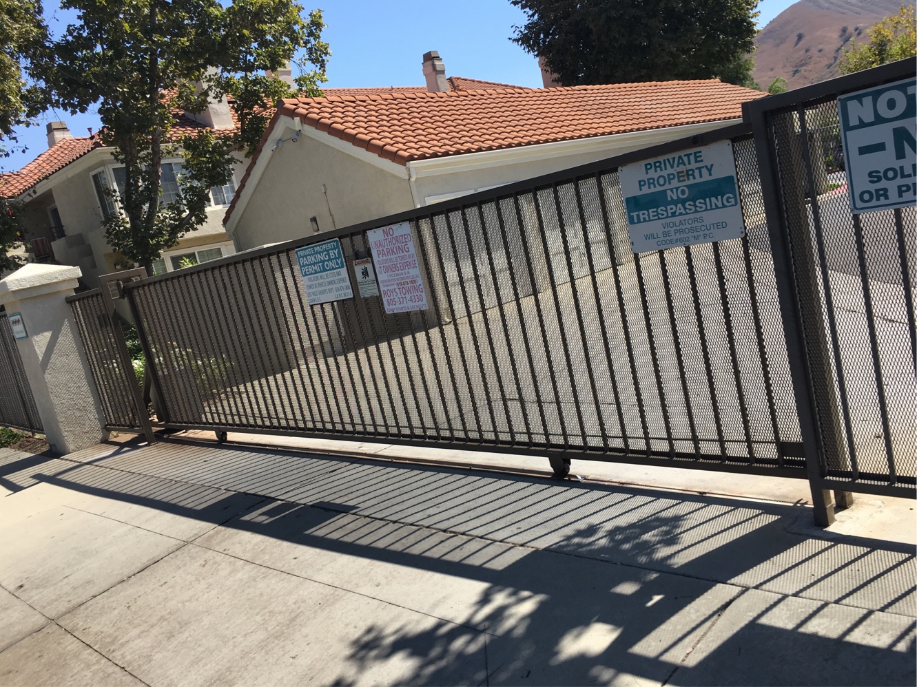 Black iron slide gate at a residential community entrance with tile-roof homes in Canoga Park, CA