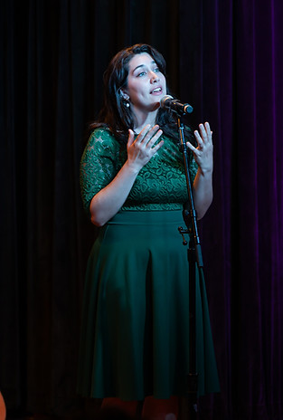 Merced is performing a duet onstage. She is in a green dress and looking towards the audience.