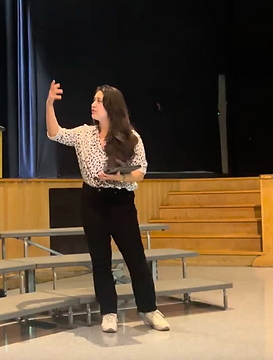 A woman in a polka dot white shirt is looking towards a student, off camera, and gesturing upward with her arm.